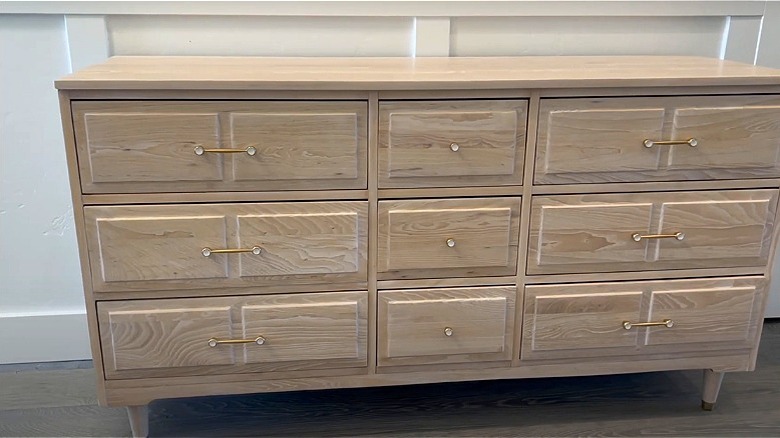 A chest of whitewashed wood drawers with gold hardware.
