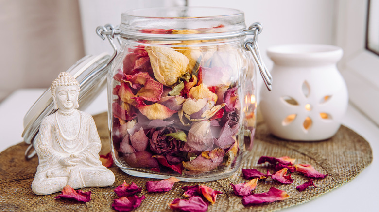 Dried flower petals in a jar near a lit candle and Buddha statue