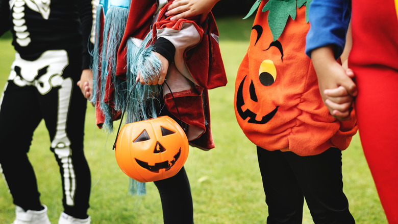 Close-up, with no faces, of kids in various Halloween costumes, including a skeleton and jack-o-lantern