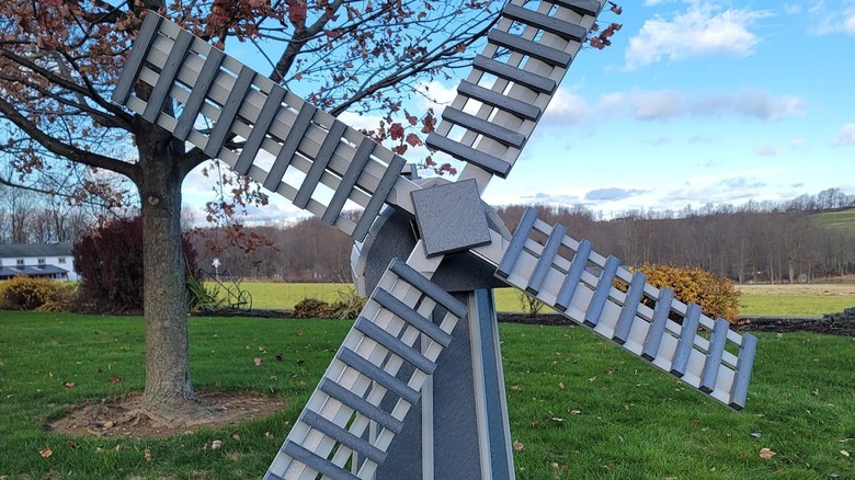 A blue and white windmill with a field and a tree in the background