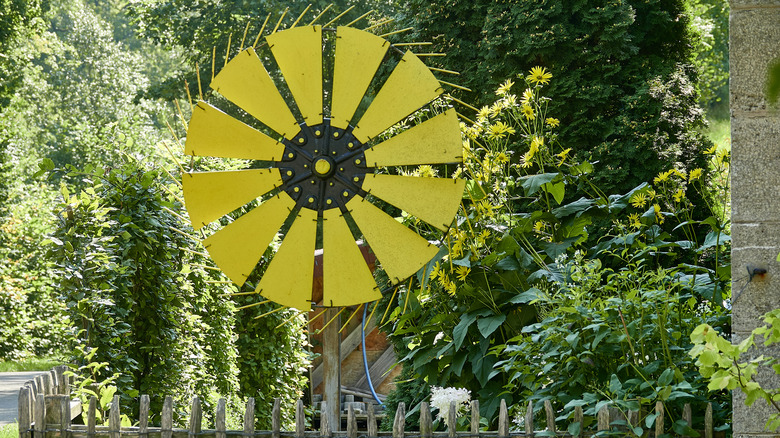 A bright yellow windmill behind a wooden fence surrounded by various greenery