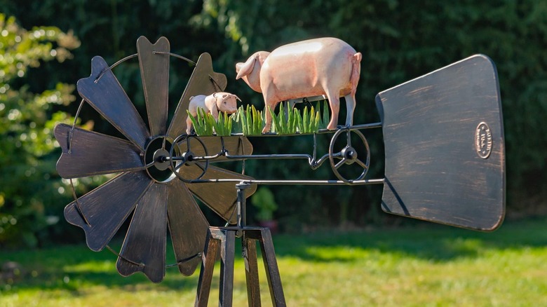 A metallic outdoor windmill with two little pigs and grass on top