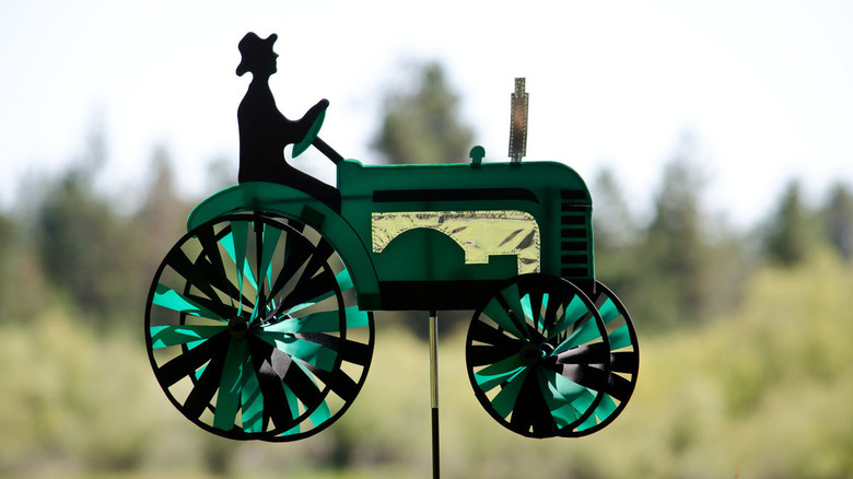 A man on a tractor with wheels that spin in the breeze on a post.
