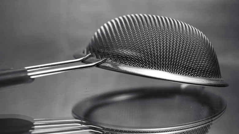 A fine mesh strainer with a handle sits upside-down on a reflective surface.