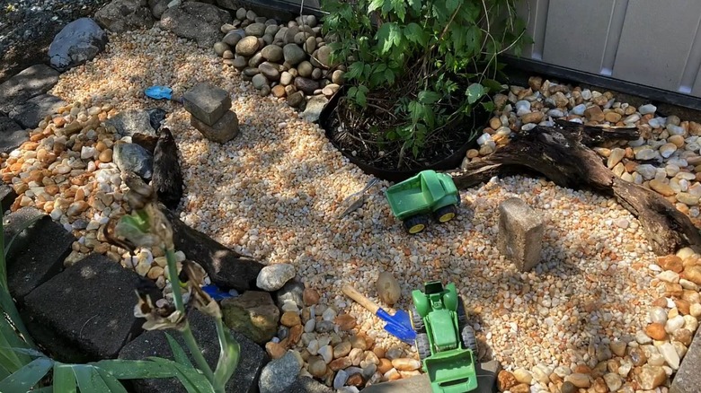 A DIY gravel rock play box with two toy trucks and a few shovels.
