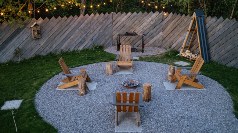 A backyard featuring a large, round fire pit area with four chairs.