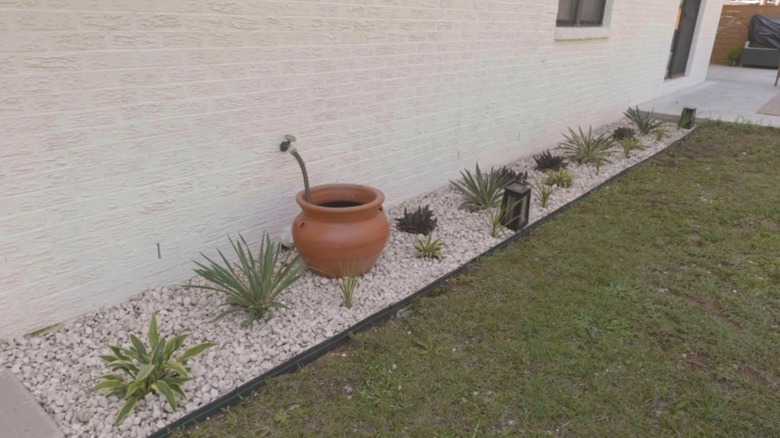 A gravel garden bed lines the side of a white brick home.