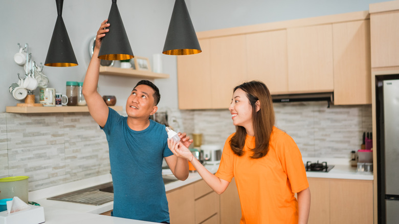 A couple installing light bulbs in kitchen