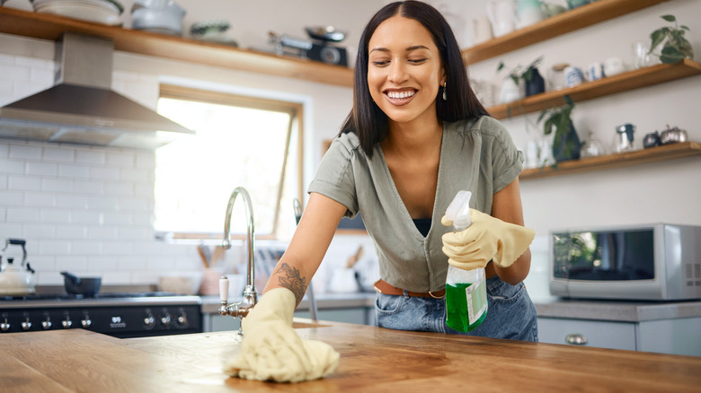 A smiling young woman cleaning a kitchen counter