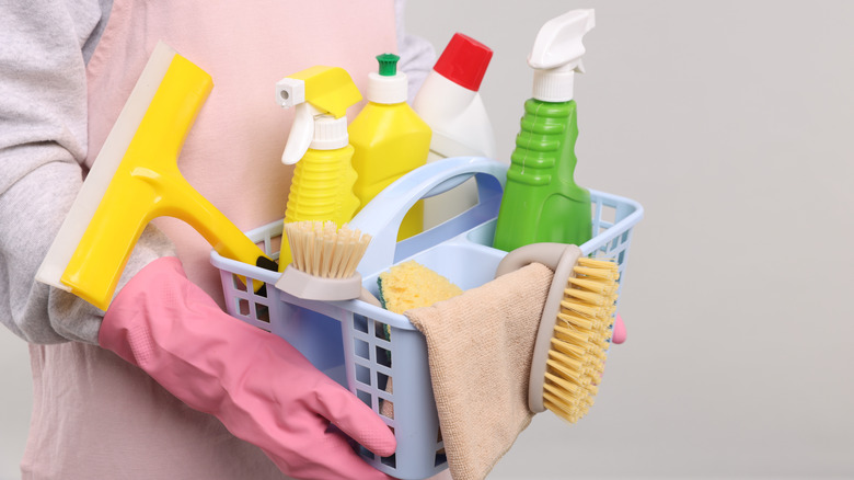 Hands with rubber gloves on holding a plastic basket of cleaning products