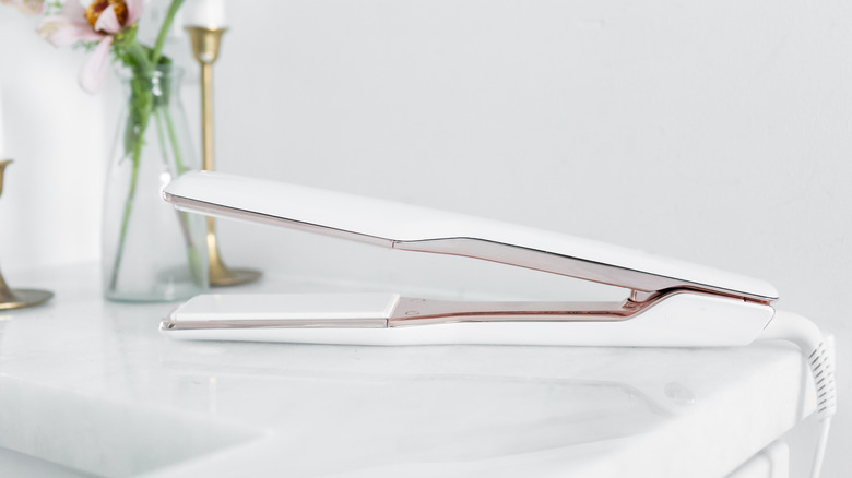 Hair straighteners lying on white marble bathroom sink.