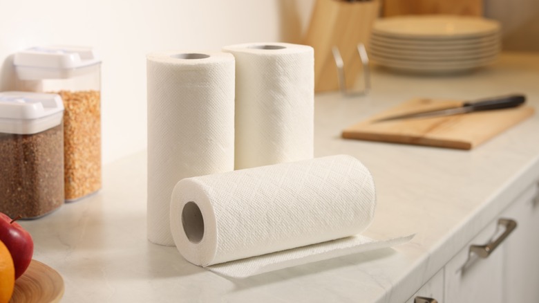 Three kitchen paper rolls on a white marble kitchen counter.