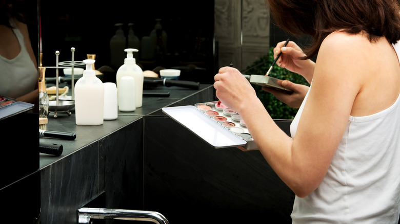 Woman applying makeup in a bathroom mirror.
