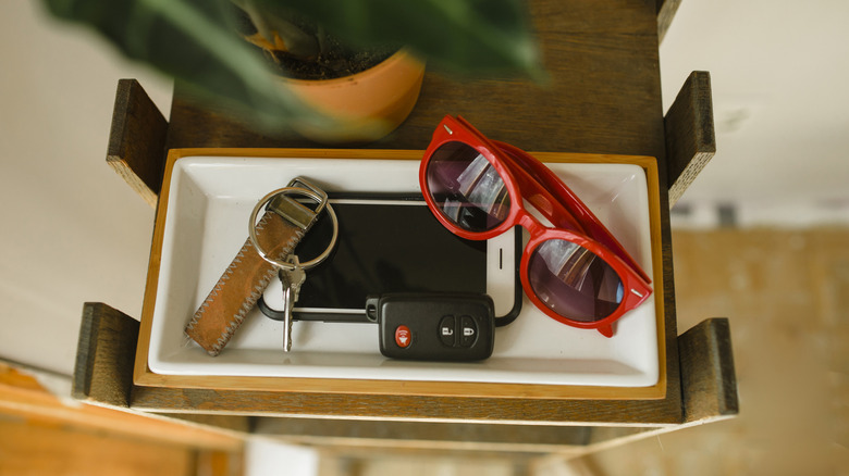white tray with phone, keys, and sunglasses on it next to a plant
