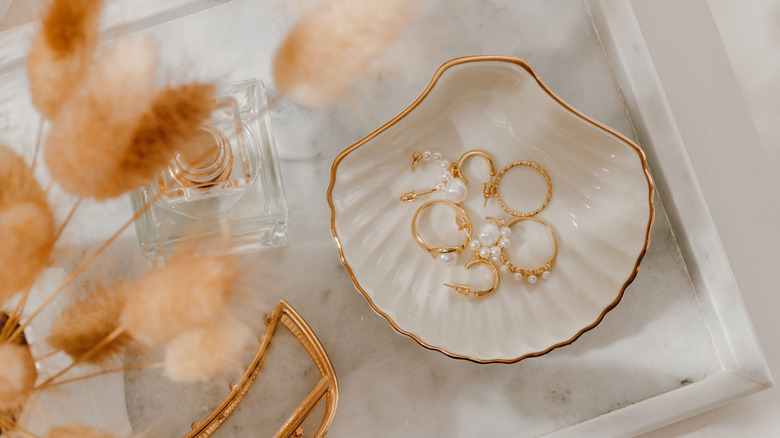 small white and gold shell tray holding gold and pearl jewelry