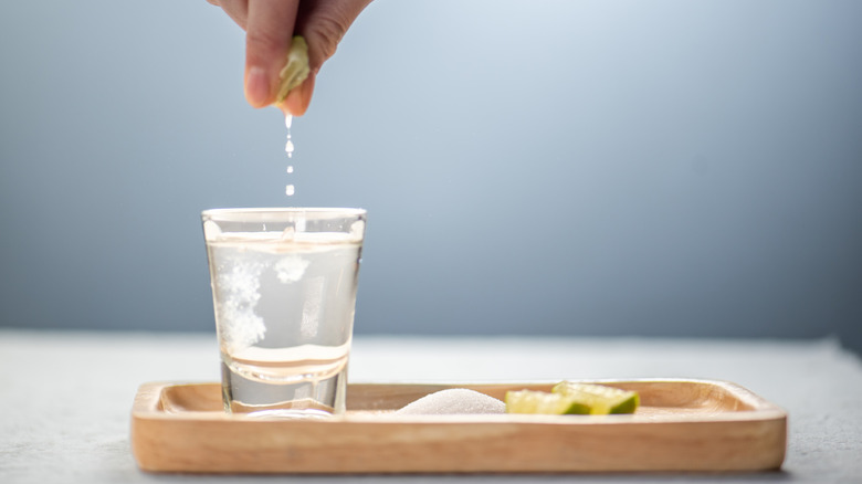 wood tray with shot glass, salt, and limes with someone squeezing lime into glass