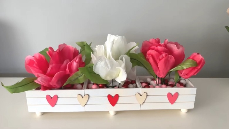 Wooden crate tray with small wooden hearts on front and artificial flowers inside