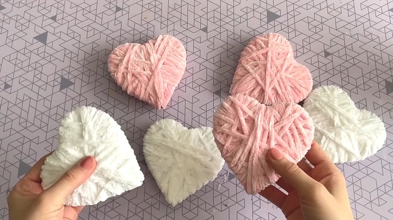 Person holding yarn-covered hearts with more in the background