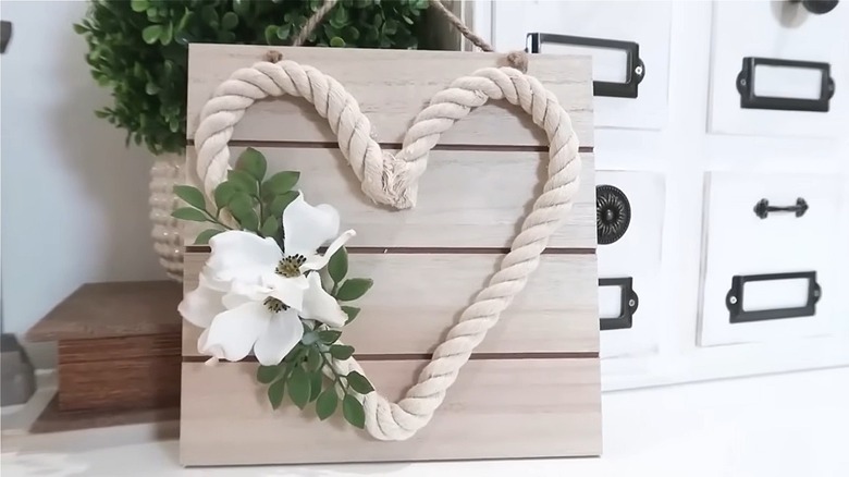 Plank background with a thick nautical rope heart and white flowers on a sign leaned against a set of white drawers