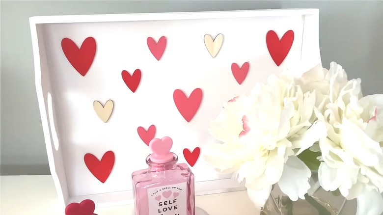White wooden tray with various colored hearts on the bottom next to perfume and flowers