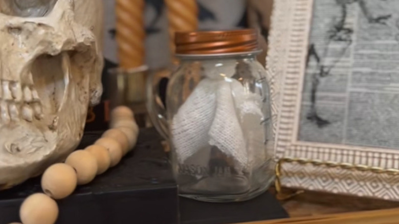 A cloth ghost inside a salt shaker on a shelf with other Halloween decorations.