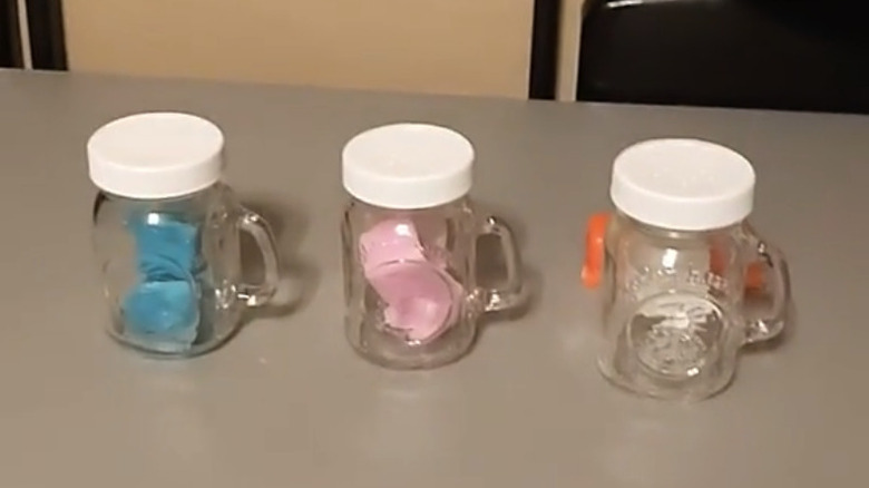 Three salt and pepper shakers on a table filled with different colored wax melts.