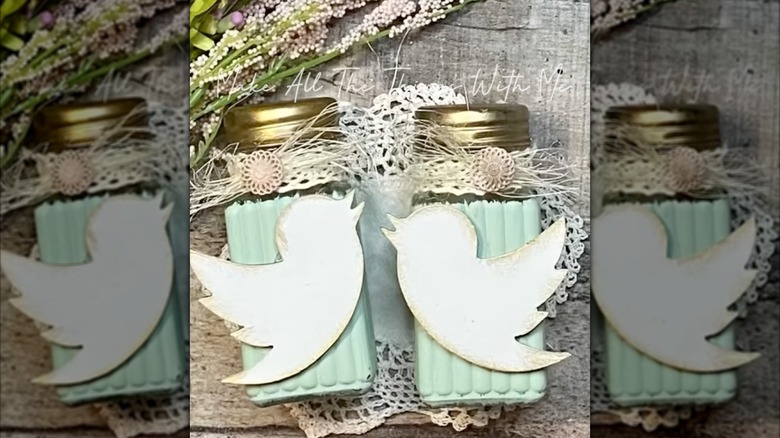 Teal and gold salt and pepper shakers with birds facing each other on a wood surface with plants.