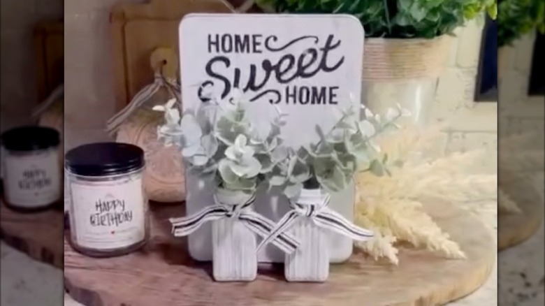 A home wweet home sign attached to painted salt and pepper shakers filled with faux foliage.