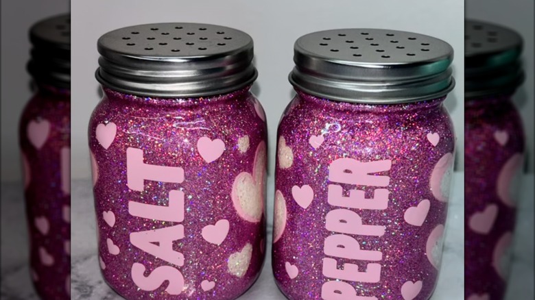 Pink sparkly, heart-adorned salt and pepper shakers with the words salt and pepper printed on them.