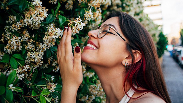 A smiling woman smelling some flowers in the street,