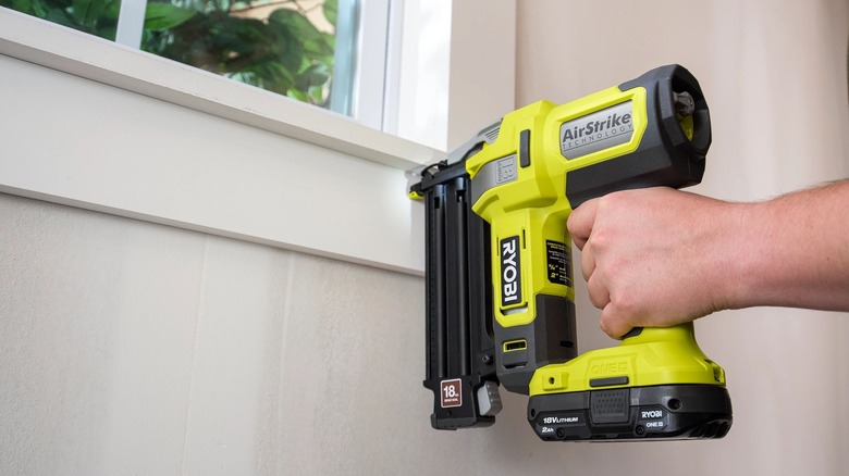 a person use a Ryobi brad nailer to attach trim around a window