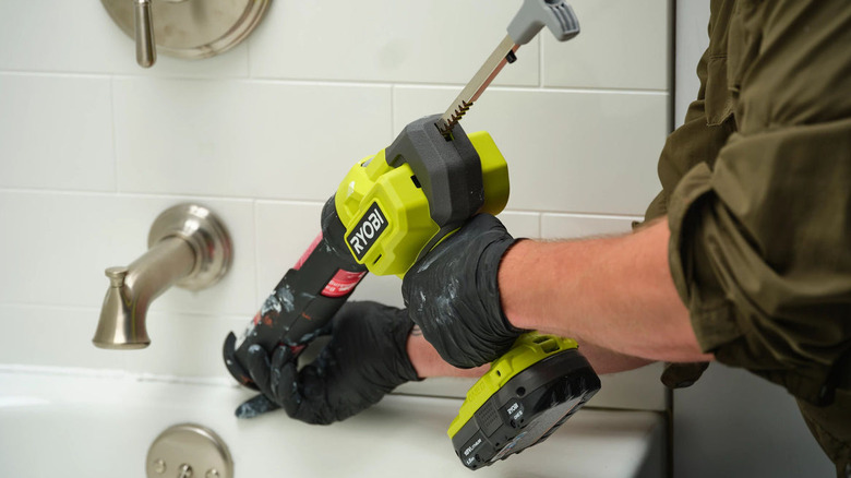 a person uses a caulk and adhesive gun to apply caulk in the bathroom