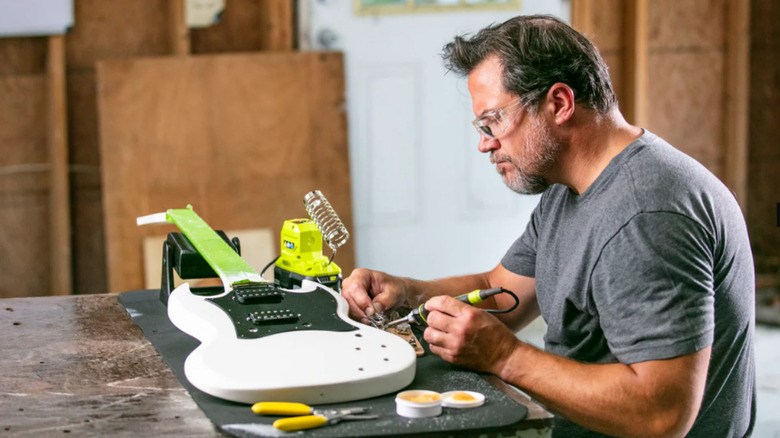 a man uses a ryobi soldering tool to work on a guitar