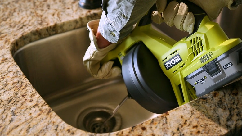 a person uses a ryobi drain auger to unclog the kitchen sink drain