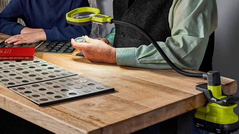 two people use a clamp on magnifying glass and light to look at a coin collection