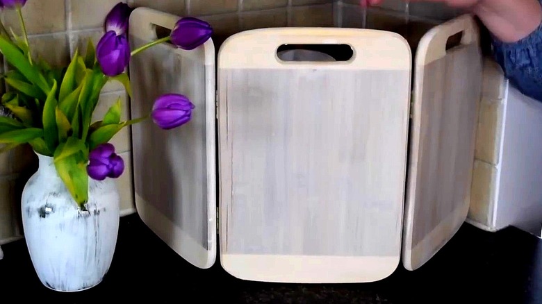 DIY hinged cutting board screen on a countertop next to a vase of purple flowers