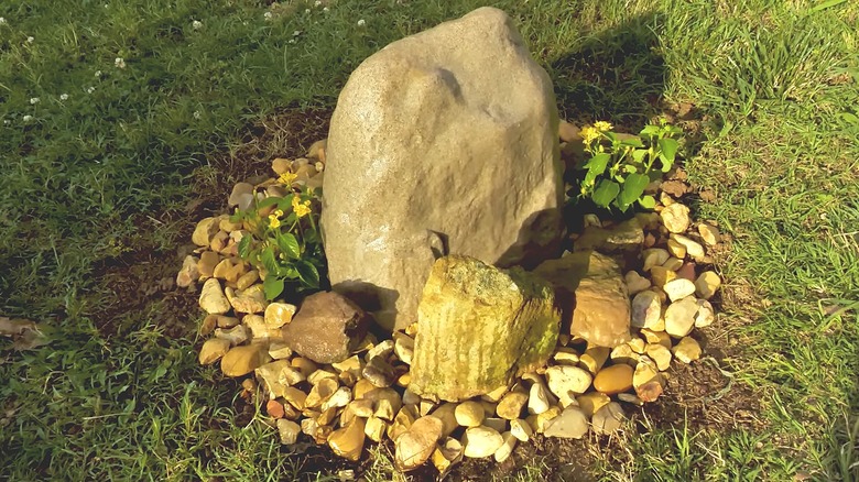 Hollow rock cover surrounded by smaller rocks to hide sewer pipe in a garden