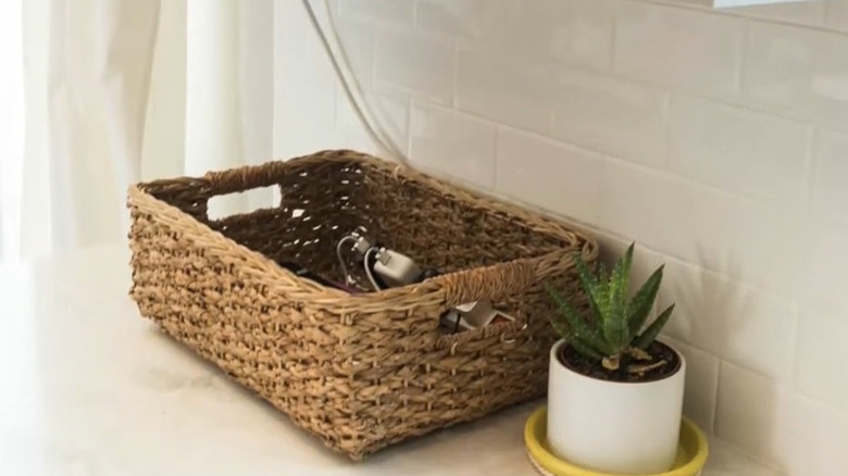 Charging station set up inside a wicker basket on a countertop next to a potted plant