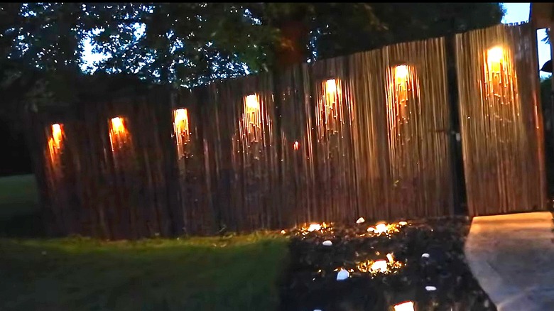 Bamboo-covered chain link fence at night with solar lights shining on it