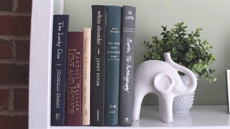 Storage container disguised with book spines sitting on a shelf next to an elephant figurine and a plant