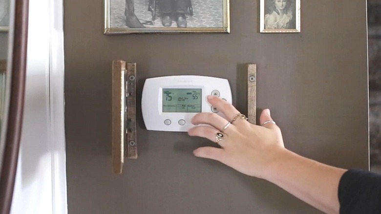 A person's hand adjusting a thermostat hanging on a wall