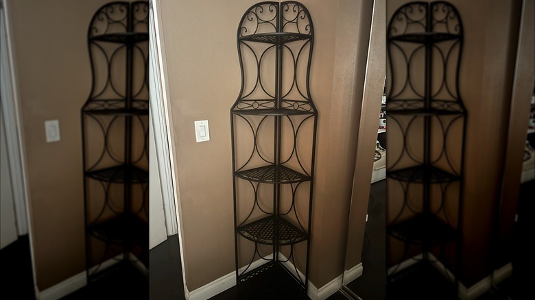Five tiered antique bronze corner shelf against a brown wall with white trim