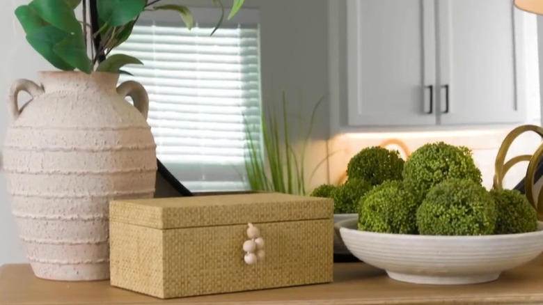 Beige storage box on a shelf in a home with a bowl of moss balls and a vase planter near it