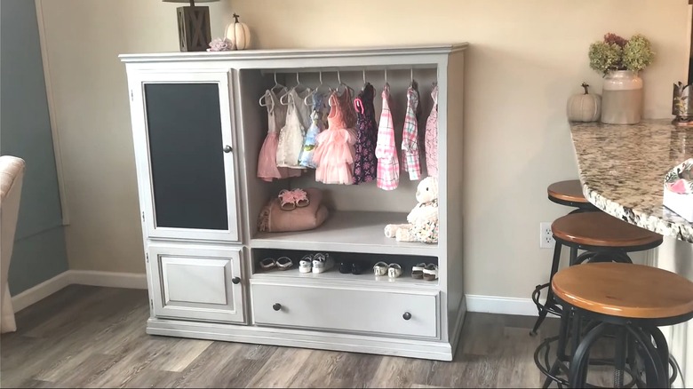 Old entertainment center converted to a child's wardrobe with clothes hanging and shoes on a shelf