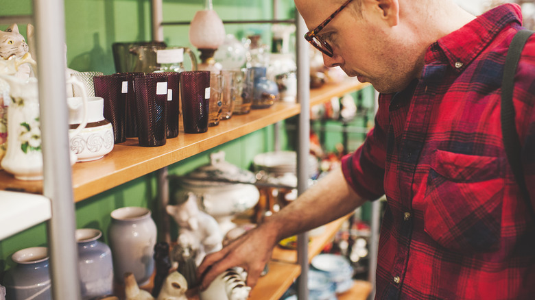Man wearing a red plaid shirt picking up an item on a shelf at a secondhand store