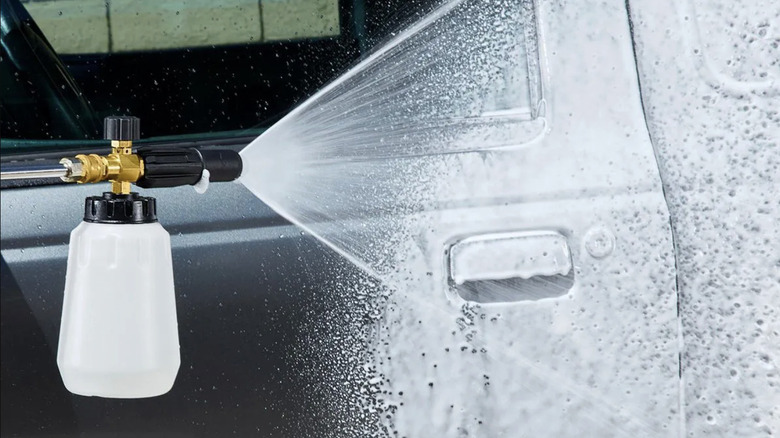 A foam cannon accessory on a pressure washer sprays soap onto a car