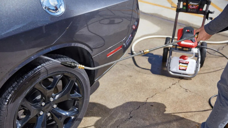 A man uses the pressure washer extension wands to clean around the tire of a car