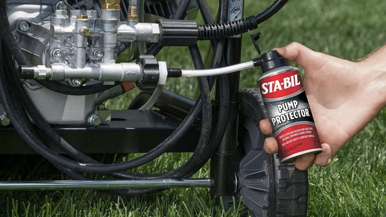 A person uses a can of STA-BIL's pump protector on a washer