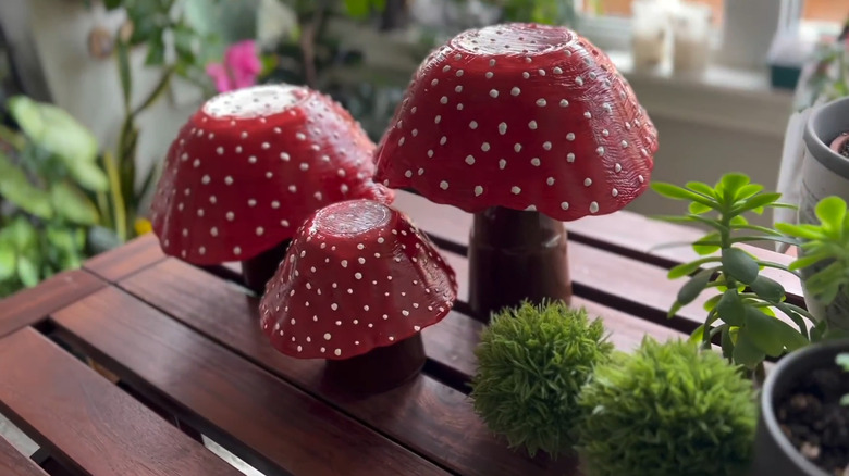 Three decorative glass mushrooms upcycled from glassware, painted red with white dots, sitting on a table