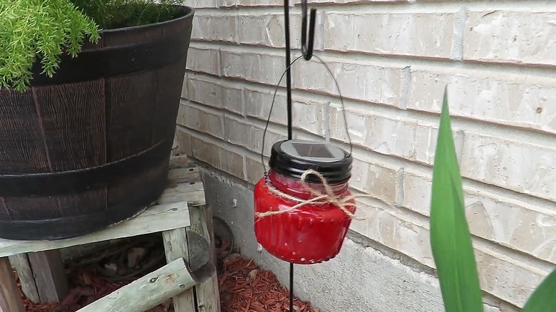 Small jar painted red with a solar light on top hanging from a small shepherd's hook